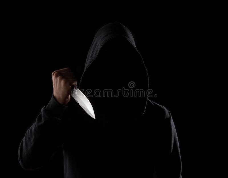 A dangerous hooded man standing in the dark and holding a shiny knife. Face can not be seen. A dangerous hooded man standing in the dark and holding a shiny knife. Face can not be seen