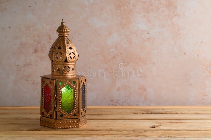 Lightened lantern on wooden table over stone wall background. Ramadan Kareem holiday celebration concept. Lightened lantern on wooden table over stone wall background. Ramadan Kareem holiday celebration concept