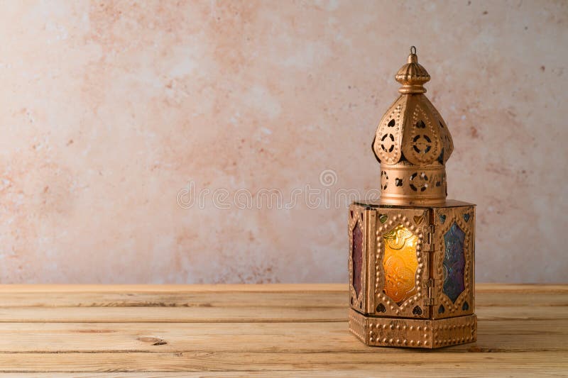 Lightened lantern on wooden table over stone wall background. Ramadan Kareem holiday celebration concept. Lightened lantern on wooden table over stone wall background. Ramadan Kareem holiday celebration concept