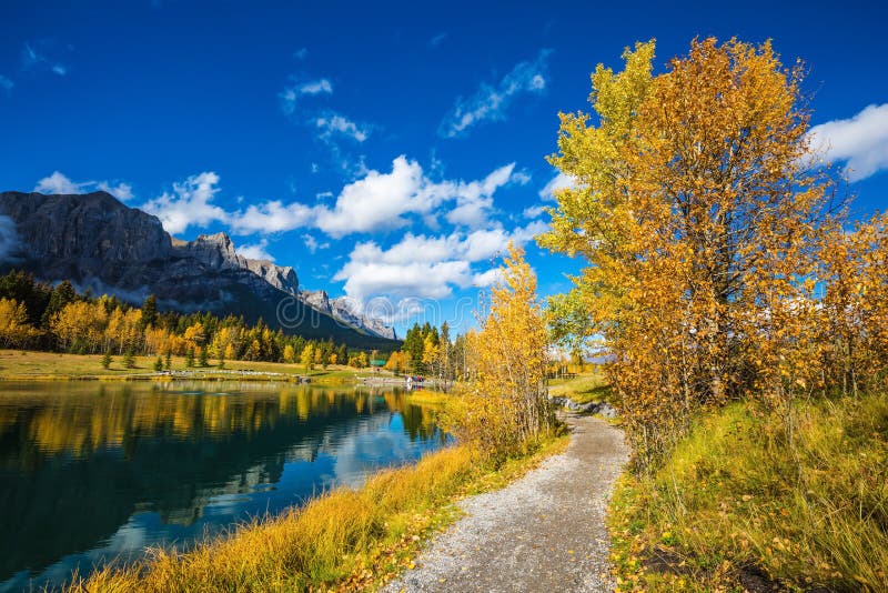 Canmore, near Banff Park. Path around the lake. The concept of hiking. Majestic mountains and autumn aspens reflected in the water. Canmore, near Banff Park. Path around the lake. The concept of hiking. Majestic mountains and autumn aspens reflected in the water