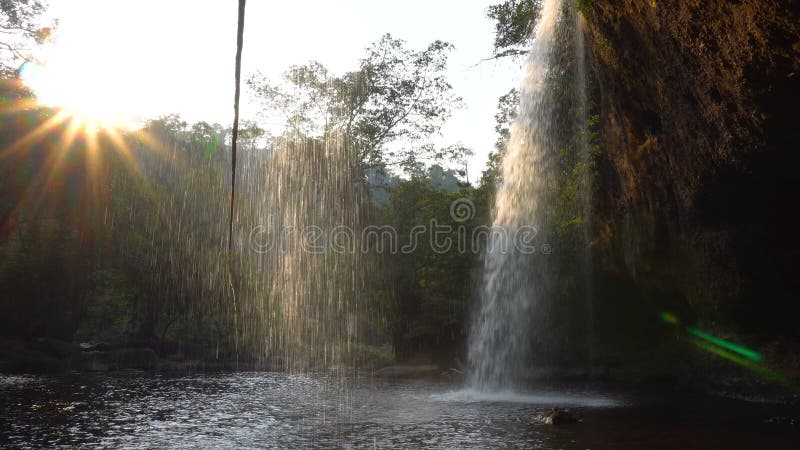 Осмотрите кафе формы под живописным водопадом в джунглях на времени вечера Вода падения в бассейн через лучи солнца на