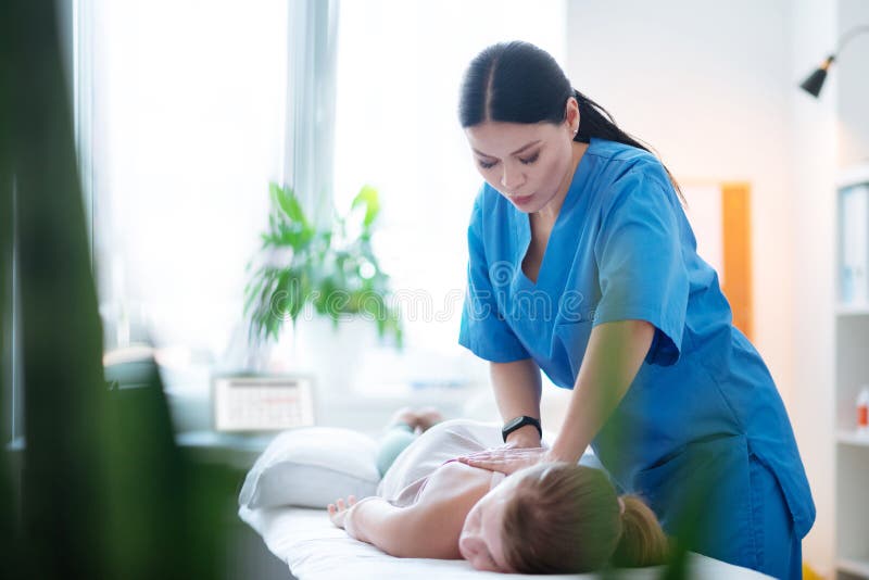 Осторожная умелая женщина быть профессиональным masseuse и работая с ребенк стоковое изображение Осторожная умелая женщина быть профессиональным masseuse и работая с ребенк стоковое изображение