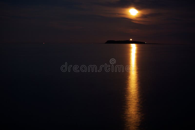 Ocean island lightened by beam of moonlight and coinciding with beam of light from lighthouse. Ocean island lightened by beam of moonlight and coinciding with beam of light from lighthouse