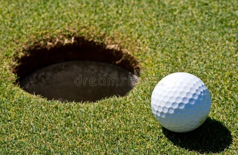 Golf ball next to a hole on a golf course. Golf ball next to a hole on a golf course