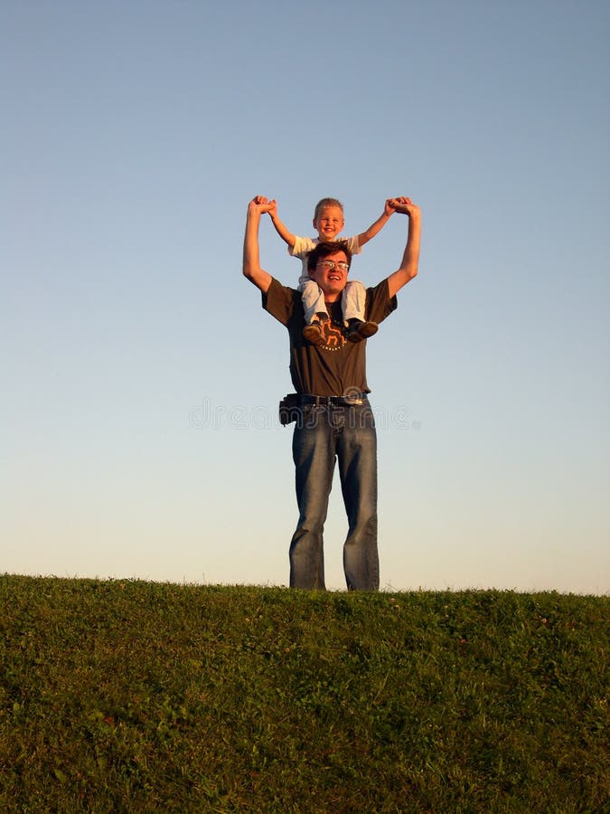 Father with son on shoulders on sundown grass sky smile. Father with son on shoulders on sundown grass sky smile