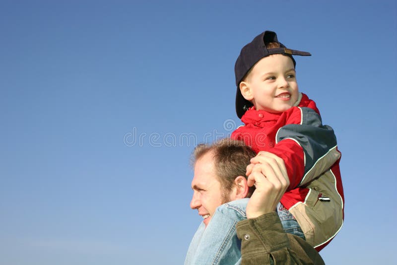 Son on father shoulders against blue sky. Son on father shoulders against blue sky