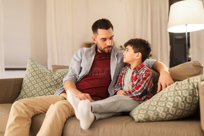 Family, relationships and trust concept - father talking to his sad little son at home in evening. Family, relationships and trust concept - father talking to his sad little son at home in evening