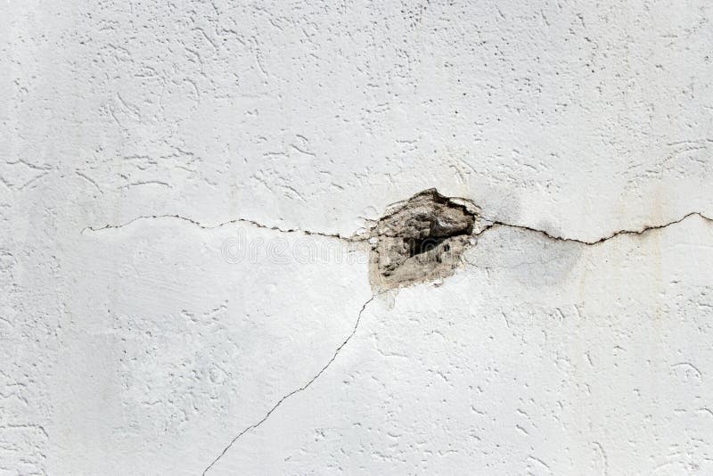 Hole and cracks in concrete white wall with copy space. Concept of damage to building. Hole and cracks in concrete white wall with copy space. Concept of damage to building