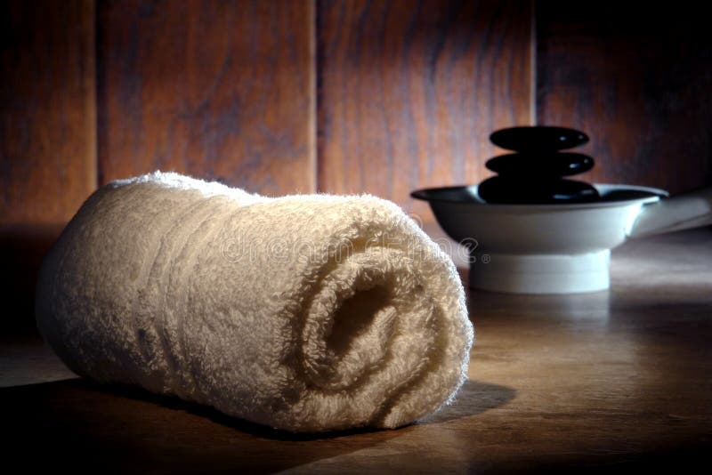 Soft white cotton towel and black polished hot massage stones cairn on a heater for a pampering relaxation treatment in a vintage style spa. Soft white cotton towel and black polished hot massage stones cairn on a heater for a pampering relaxation treatment in a vintage style spa