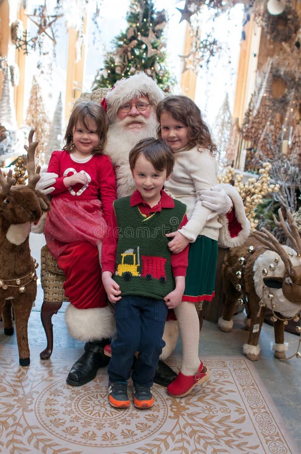 View of 3 Siblings, 2 girls and 1 boy sitting on Santa with decorated tree in background. View of 3 Siblings, 2 girls and 1 boy sitting on Santa with decorated tree in background