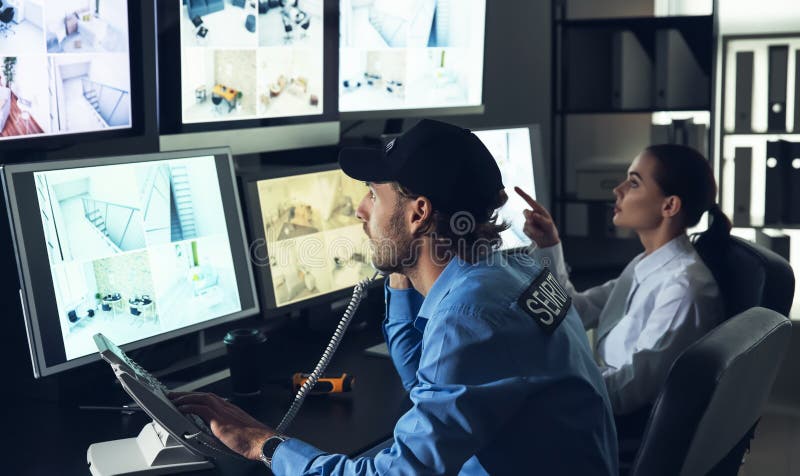 Охранники контролируя современные камеры CCTV в комнате наблюдения стоковое фото