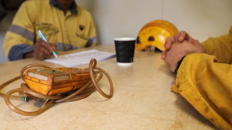 Defocused isolated construction worker Asian hand written Job Hazard Analysis JHA risk assessment on the table when working on confined restricted space with gas tester atmosphere on the foreground. Defocused isolated construction worker Asian hand written Job Hazard Analysis JHA risk assessment on the table when working on confined restricted space with gas tester atmosphere on the foreground