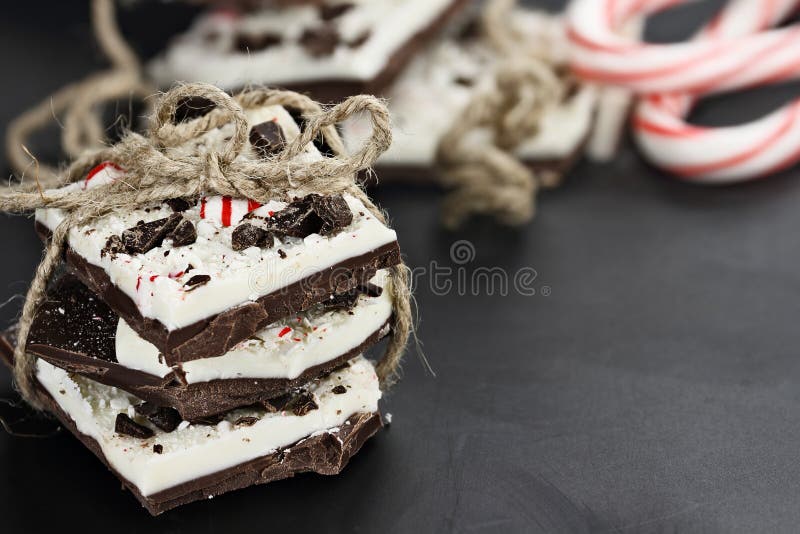 Dark and white chocolate peppermint bark stacked and tied together over a black background. Extreme shallow depth of field with selective focus on ribbon. Dark and white chocolate peppermint bark stacked and tied together over a black background. Extreme shallow depth of field with selective focus on ribbon.