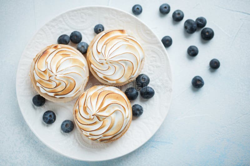 Очень вкусные tartlets лимона с меренгой на белой винтажной плите Сладостное обслуживание на свете - голубая предпосылка Плоское стоковое фото rf Очень вкусные tartlets лимона с меренгой на белой винтажной плите Сладостное обслуживание на свете - голубая предпосылка Плоское стоковое фото rf