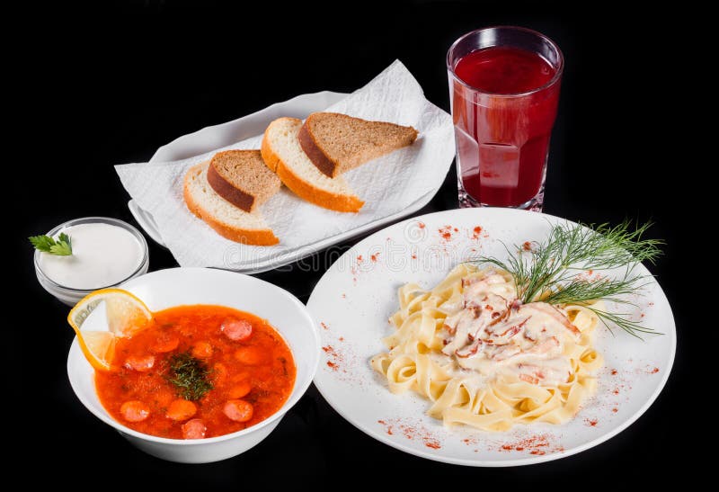 Очень вкусный обеденный стол с макаронными изделиями Fettuccine с мясом, горячим супом с сосисками, хлебом и компотом на черноте стоковое фото Очень вкусный обеденный стол с макаронными изделиями Fettuccine с мясом, горячим супом с сосисками, хлебом и компотом на черноте стоковое фото