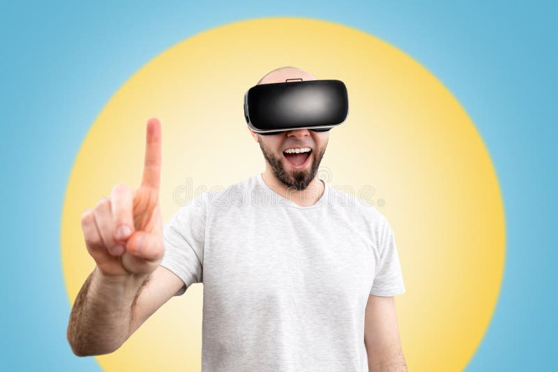 очки vr. удивившийся человек в очках виртуальной реальности с чуть открытым ртом показывает пальцем в космос. синий фон стоковое фото