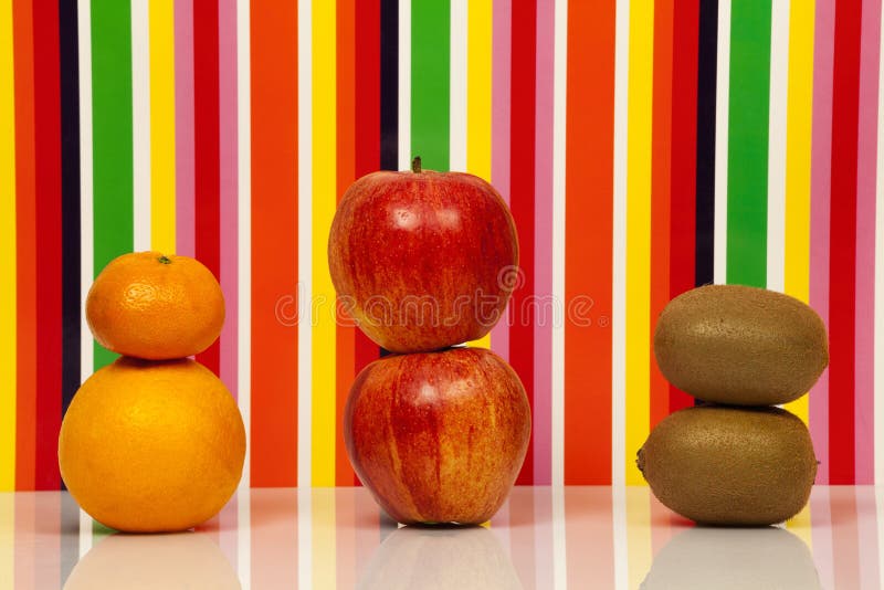 Two apples, an orange, a tangerine, two Kiwis are on a glossy surface with a background behind multicolored. Two apples, an orange, a tangerine, two Kiwis are on a glossy surface with a background behind multicolored.