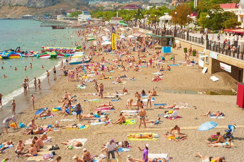 Пляж Крыма в лете. SUDAK, УКРАИНА - SEPT. 08, 2015: Люди на пляже моря в Sudak Согласно национальное географическому, Крым находился среди назначений перемещения 20 лучших в 2013