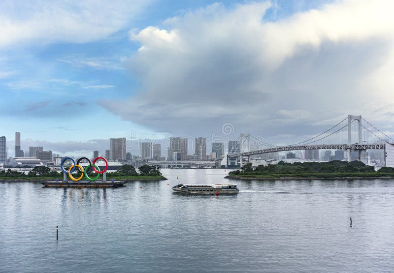 памятник олимпийских колец с водным автобусом, плывущим перед радужным мостом.