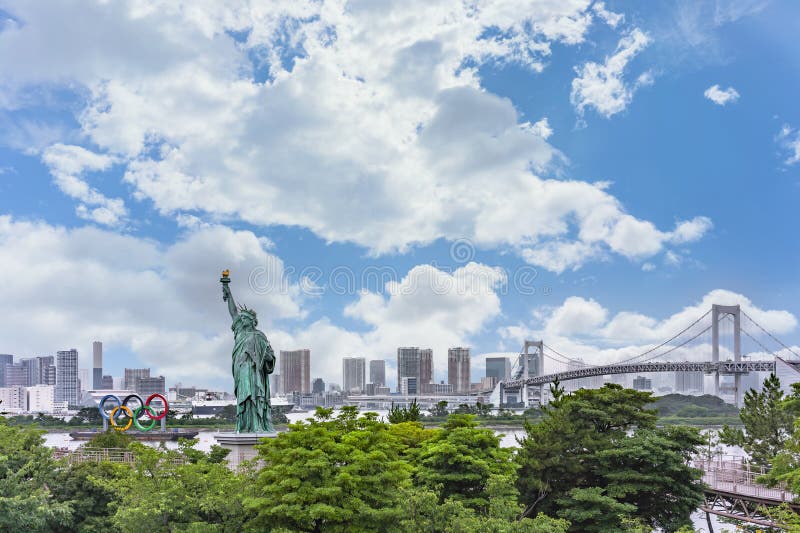 памятник статуе свободы и олимпийским кольцам токио перед радужным мостом.