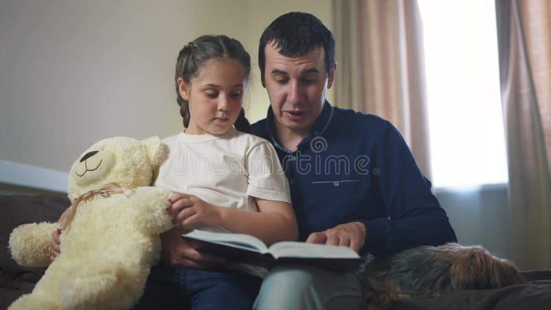 Папа читает книгу дочери в спальне. счастливая семейная мечта. отец-родитель читает книгу ночью