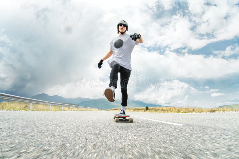 Парень в шлеме и солнечных очках ускоряет ход нажатия его ноги на его longboard стоковое фото