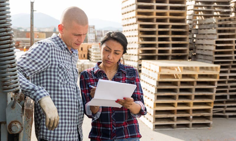 Confident woman manager discussing order list with man worker at warehouse of building materials. Confident woman manager discussing order list with man worker at warehouse of building materials