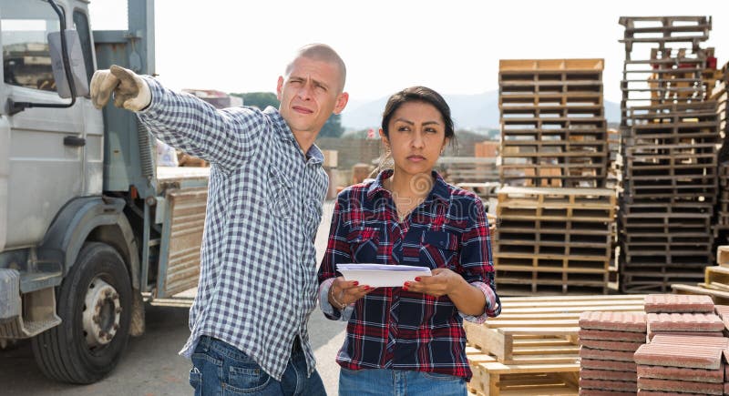 Confident woman manager discussing order list with man worker at warehouse of building materials. Confident woman manager discussing order list with man worker at warehouse of building materials