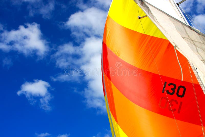 Brightly colored sail against a blue sky with white puffy clouds. Brightly colored sail against a blue sky with white puffy clouds.