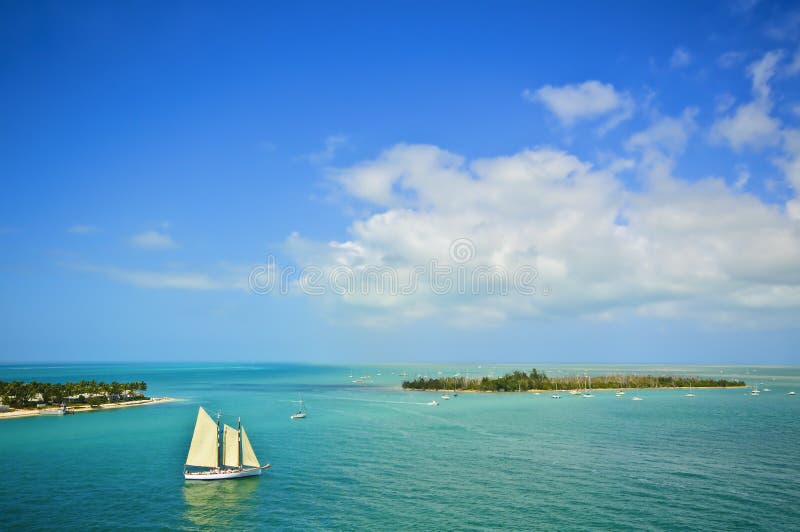 A large white sailboat with three sails approaches an island in the turquoise blue waters of the islands, or Keys, located off the coast of the southern tip of Florida as seen from Key West, a major tourist destination in the United States. A large white sailboat with three sails approaches an island in the turquoise blue waters of the islands, or Keys, located off the coast of the southern tip of Florida as seen from Key West, a major tourist destination in the United States.