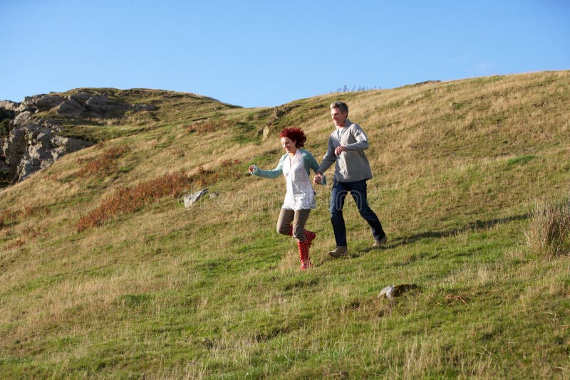 Couple in countryside running down a hill having fun. Couple in countryside running down a hill having fun