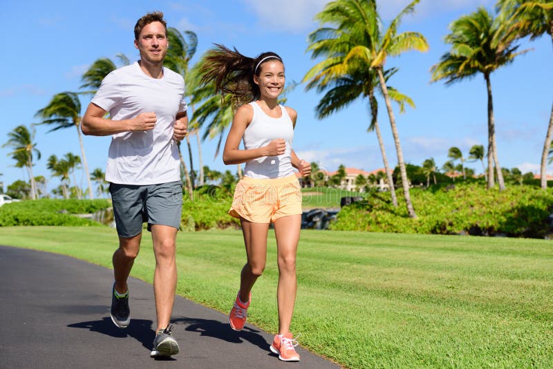 Sport couple exercising running outside on street in summer. Happy active young fit adults jogging together with tropical background in city park or resort road. Asian and Caucasian people. Sport couple exercising running outside on street in summer. Happy active young fit adults jogging together with tropical background in city park or resort road. Asian and Caucasian people.