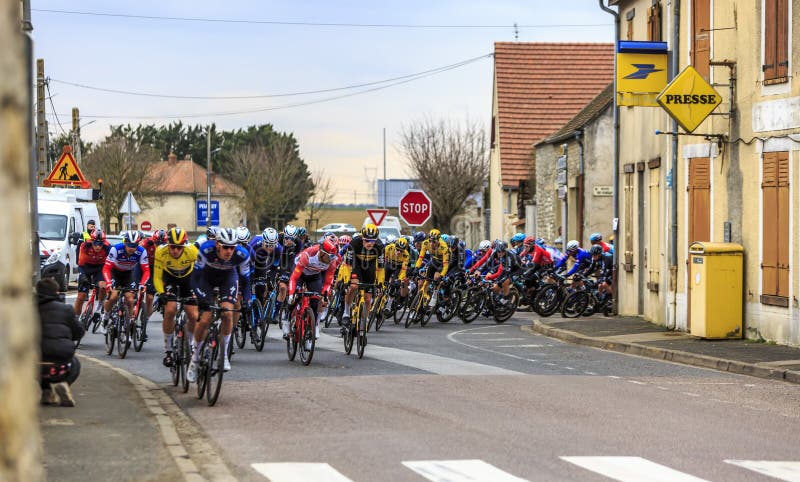 Monnerville, France - March 05, 2023: The peloton takes a bend in a small French village during Paris-Nice 2023. Monnerville, France - March 05, 2023: The peloton takes a bend in a small French village during Paris-Nice 2023