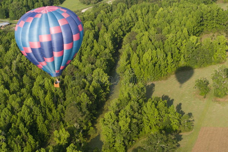 Aerial view of a hot air balloon drifting over a forested area- balloon's shadow on the ground. Aerial view of a hot air balloon drifting over a forested area- balloon's shadow on the ground