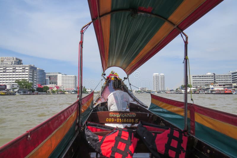 Перемещение вдоль Chao Рекы Phraya на длинной туристской шлюпке Водитель сидит во фронте и говорит на телефоне стоковое фото Перемещение вдоль Chao Рекы Phraya на длинной туристской шлюпке Водитель сидит во фронте и говорит на телефоне стоковое фото
