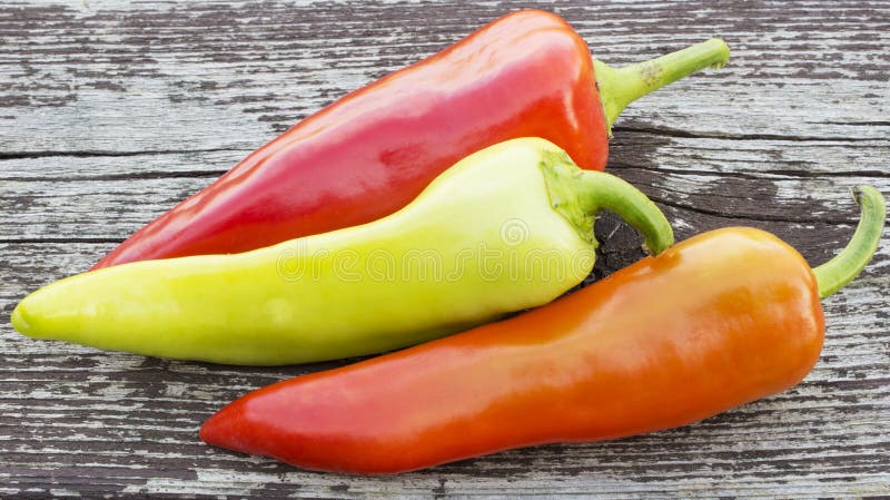 Three brightly colored banana chili peppers against an old weathered wood background. Three brightly colored banana chili peppers against an old weathered wood background.