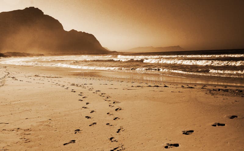 Footprints in the sand on the beach. Shot on a sunny day with a mountain in the background. Footprints in the sand on the beach. Shot on a sunny day with a mountain in the background