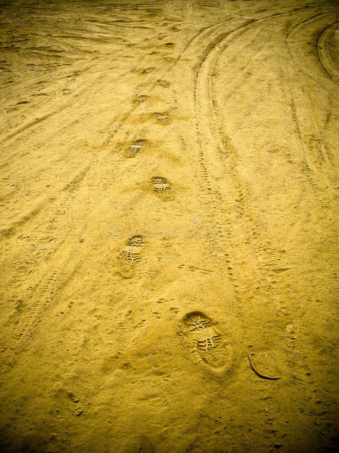 A view of footprints and tire marks in sand. Vignetting visible around the edges. A view of footprints and tire marks in sand. Vignetting visible around the edges.