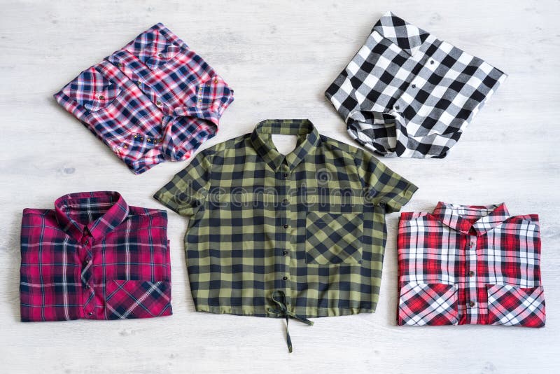 Five multi-colored checkered women`s shirts lying neatly folded on a light wooden background. Five multi-colored checkered women`s shirts lying neatly folded on a light wooden background