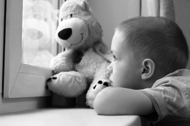 Печальный мальчик у окна и медвежья игрушка, одиночество и депрессия стоковое фото