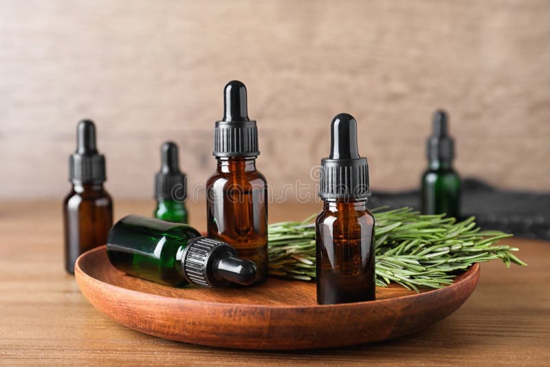 Plate with bottles of essential oils and rosemary on wooden table. Plate with bottles of essential oils and rosemary on wooden table