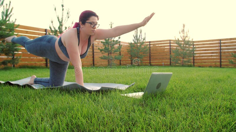 плюс женщина, занимающаяся йогой в интернете в саду на улице. занятие спортом дома в соответствии с руководством или онлайн-учебни