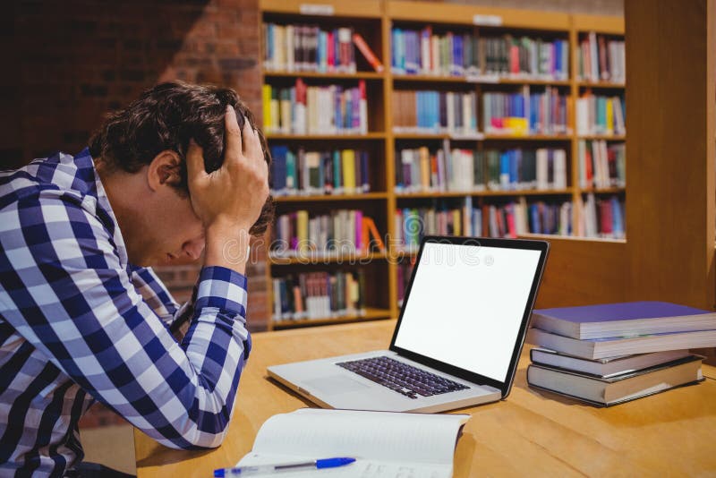 Подавленный студент сидя в библиотеке с компьтер-книжкой в коллеже