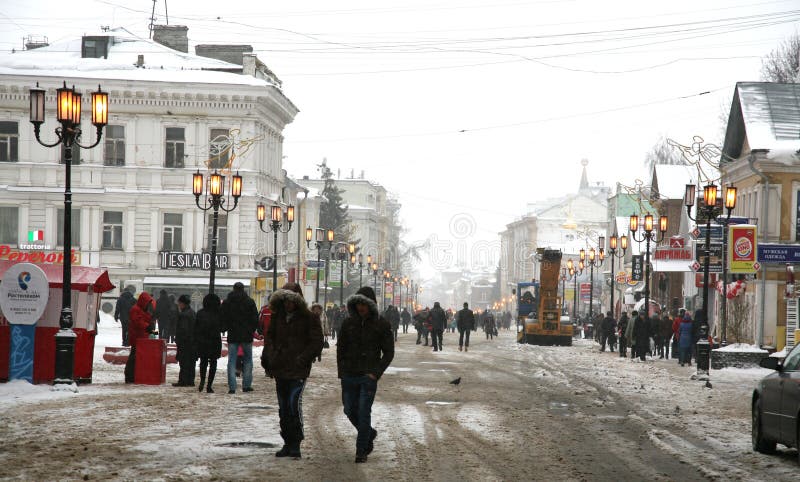 Nizhny Novgorod, Россия - 5-ое января 2015: Подвергните удаление механической обработке снега в погоде зимы ненастной на центральной исторической улице Bolshaya Pokrovskaya пешехода В праздниках Нового Года много людей идут и видят украшения рождества