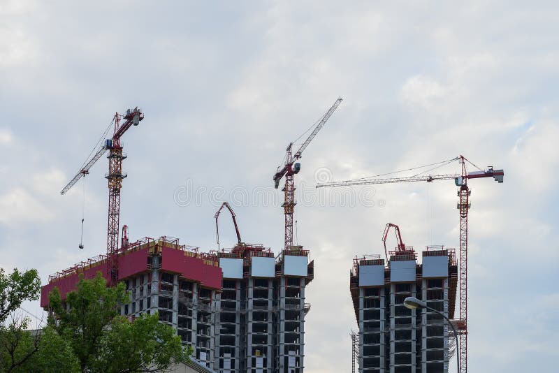 Поднимите краны башни на строительной площадке против предпосылки голубого неба, здания домов новые около жилого района стоковое изображение Поднимите краны башни на строительной площадке против предпосылки голубого неба, здания домов новые около жилого района стоковое изображение