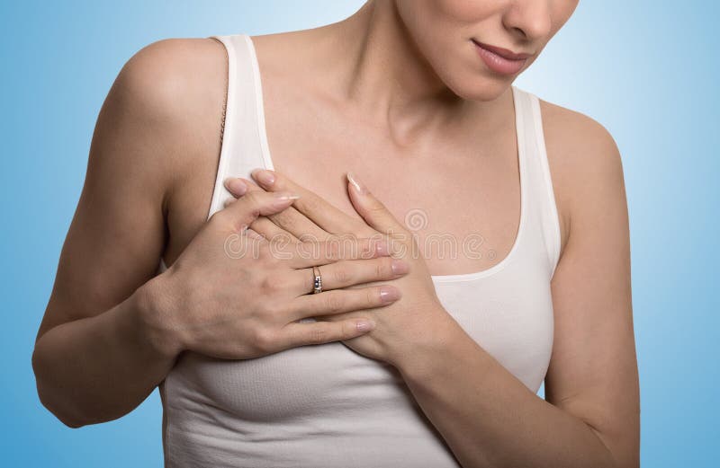 Closeup cropped portrait young woman with breast pain touching chest colored isolated on blue background. Closeup cropped portrait young woman with breast pain touching chest colored isolated on blue background