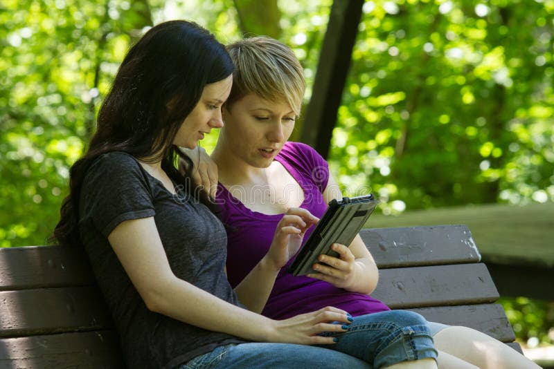 Подруги деля etablet на скамейке в парке, горизонтальной стоковые фото