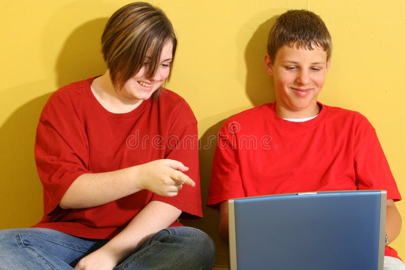 Fourteen year old boy and girl teens sitting against wall with laptop. Fourteen year old boy and girl teens sitting against wall with laptop.