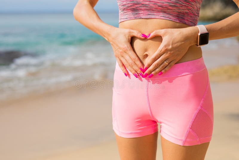 Fit woman in pink sport wear showing hands heart sign on her stomach. Fit woman in pink sport wear showing hands heart sign on her stomach