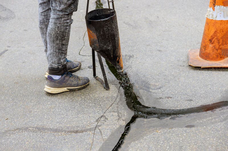 Man sealing asphalt driveway with filled cracks sealcoating selective focus. Man sealing asphalt driveway with filled cracks sealcoating selective focus